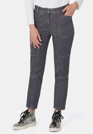 Pantaloni in denim grigio con design aderente, dotati di multiple tasche e cuciture evidenti. Abbinati a sneakers argentate riflettenti con lacci neri.
