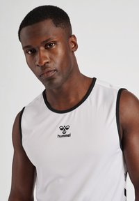 Sports tank top i hvid med sort trim, lavet af åndbart stof. Har et logo på brystet og ærmeløs design for nem bevægelse.