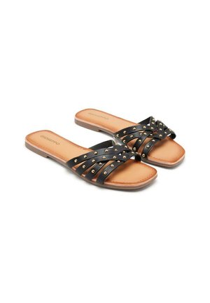 Sandales noires avec des brides entrecroisées ornées de clous dorés, semelle plate et semelle intérieure lisse marron, conçues pour un enfilage facile.