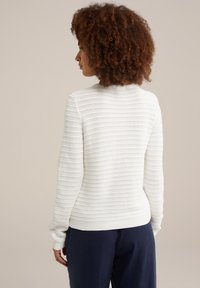 Vit, texturerad tröja med horisontella ränder, rundad halsringning och ribbat avslut i ärmar och nederkant, i kombination med mörkblå byxor.
