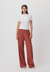 Top bianco a maniche corte abbinato a pantaloni larghi color ruggine, con una texture liscia e una cintura elastica per il comfort.