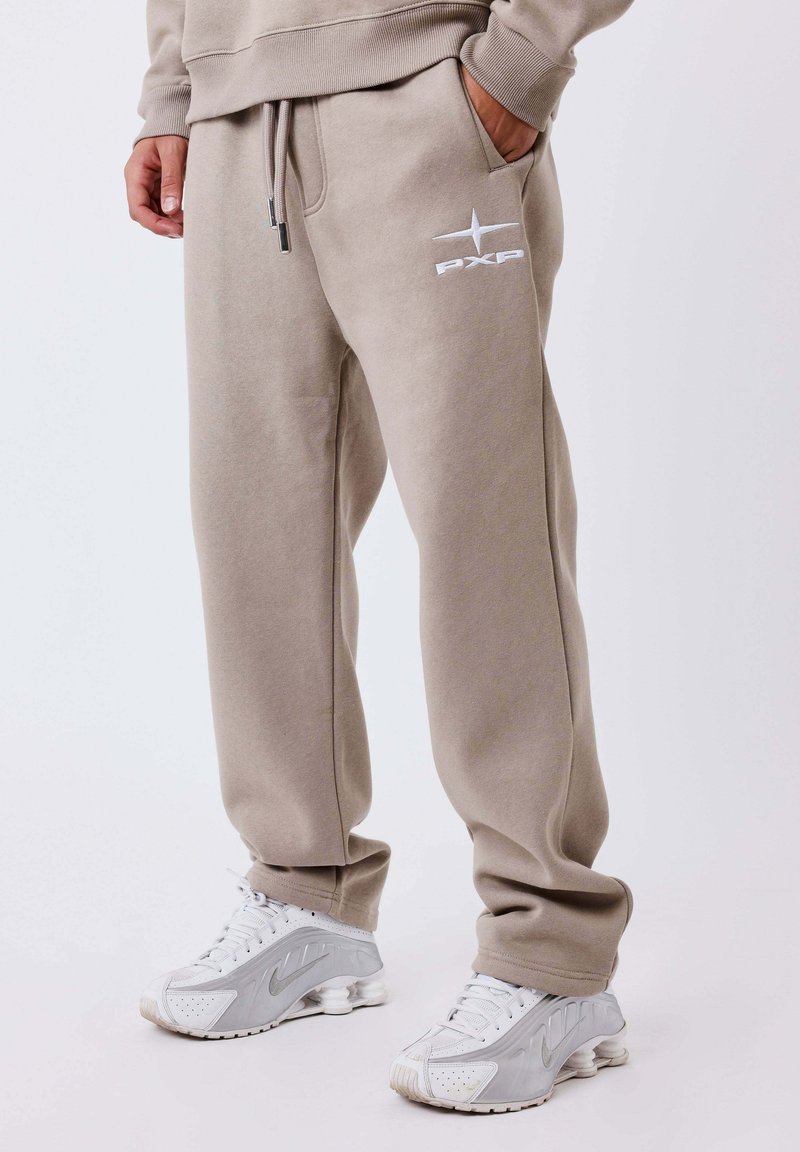 Beige sweatpants with elastic waistband and drawstring; features side pockets and white logo; paired with gray sneakers. Smooth texture.