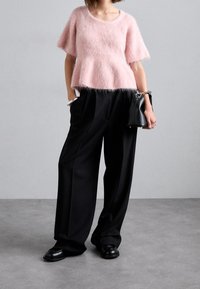 Světlý růžový chlupatý pletený top s krátkými rukávy, zkombinovaný s vysokými černými kalhotami a černými botami. Jednoduchá kabelka se stříbrným kováním.