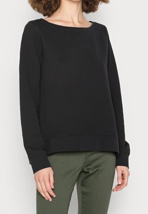 Sudadera negra de manga larga con cuello redondo, hecha de una tela suave, con puños acanalados y un ajuste relajado, combinada con pantalones verdes.