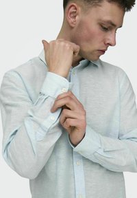 Lichtblauwe button-up shirt gemaakt van een geweven stof. Heeft lange mouwen met knopenmanchetten en een traditionele kraag.