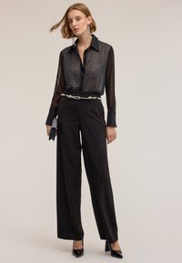 Sort gennemsigtig bluse med et geometrisk mønster, parret med høj talje sorte vide bukser og sorte hæle. Sølv bælte til accent.