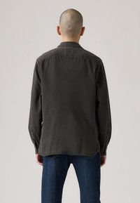 Tmavosivá košeľa s dlhými rukávmi, golierom, gombíkovými manžetami a rovný lem, prezentovaná na osobe nosiacej modré džínsy.