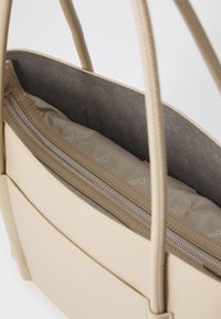 Borsa in pelle beige con doppie cinghie per le spalle, caratterizzata da un'esterno liscio, un compartimento con zip e una fodera interna grigia.