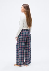 Μπλουζάκι με μακριά μανίκια σε ανοιχτό μπεζ χρώμα, σε συνδυασμό με φαρδιά παντελόνια καρό σε μπλε ναυτικό, με κόκκινες, πράσινες και λευκές γραμμές. Μαλακό ύφασμα, άνετη εφαρμογή.