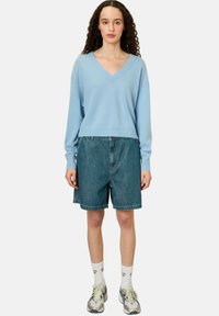 Un pull v-neck bleu clair, doux, associé à un short en denim. Le short a une coupe ample et des ourlets repliés, complété par des chaussettes blanches et des baskets.