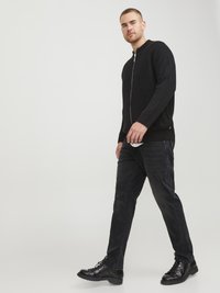 Suéter negro de canalé con cremallera y cuello redondo, combinado con jeans oscuros y botas negras de cordones, creando un aspecto monocrático elegante.