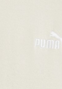 Világos bézs színű, sima textúrájú pamut anyag, fehér hímzett "PUMA" logóval és kis futó puma ikon mellett.
