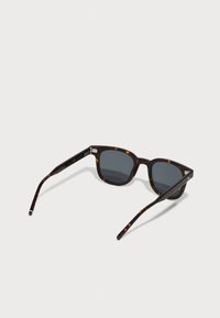 Lunettes de soleil écaille de tortue avec verres gris. Forme carrée, branches fines avec une légère courbure, et un détail de charnière en métal. Texture lisse sur l'ensemble.