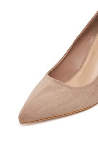 Zapato plano de mujer en ante beige con punta puntiaguda, interior de cuero suave y suela de color marrón claro.