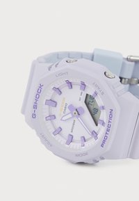 G-SHOCK klokke i lys lilla med rund hus, digital og analog skjerm, lilla detaljer og silikonrem. Vanntett opptil 20 bar.