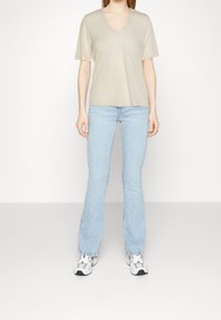 Beige V-udskæring T-shirt med korte ærmer, parret med lysblå flagrende jeans og hvide sneakers med sorte accenter. Glat stoftekstur.