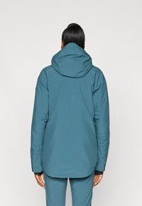 Merev teal värvi välistingimustes jacket kapuutsiga, millel on sile tekstuur ja veidi pikenenud selja serv. Valmistatud veekindlast materjalist.