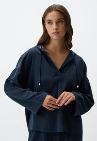 Felpa con cappuccio blu navy a V, maniche lunghe e cordini regolabili al collo. Tessuto liscio con vestibilità rilassata.