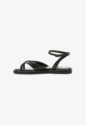 Black leather sandal with a thin ankle strap, open-toe design, and flat sole. Crossed straps create a modern silhouette. Smooth texture.