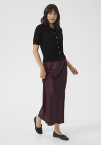 Black short-sleeve cardigan with buttons, paired with a burgundy satin maxi skirt and black flats with a bow detail.