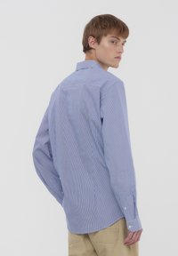 Camicia a maniche lunghe a righe blu realizzata in cotone leggero. Presenta un colletto classico, polsini con bottoni e un orlo curvo.