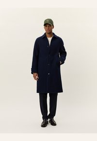Navy blue wool overcoat with a classic design, featuring a button front, two side pockets, and a notched collar. Worn over a light shirt.