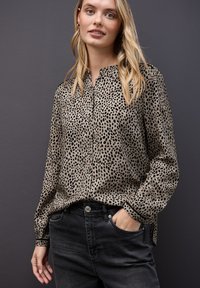 Blusa beige con stampa leopardata, colletto, apertura con bottoni e maniche lunghe, abbinata a jeans denim neri. Tessuto liscio.