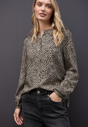 Blusa beige con stampa leopardata, colletto, apertura con bottoni e maniche lunghe, abbinata a jeans denim neri. Tessuto liscio.