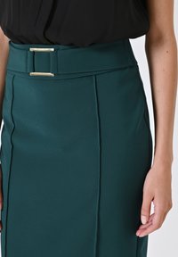 Gonna a matita teal con una texture liscia, dotata di una cintura larga e di un accentuato fibbia rettangolare argentata nella parte davanti.