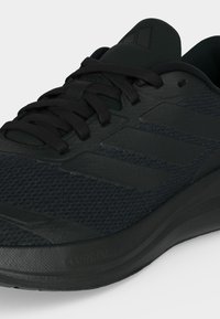 Baskets de sport noires avec tige en mesh, trois bandes latérales texturées, lacets noirs, languette rembourrée et semelle amortissante portant la mention "cloudfoam".