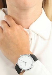 Runder Silberner Uhr mit einem weißen Zifferblatt, schwarzem Lederarmband, minimalistischem Design, dünnen Stundenmarkierungen und Datumsanzeige um 6 Uhr.