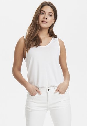 Weißes ärmelloses Oberteil mit einem runden Ausschnitt, aus weichem Stoff; kombiniert mit weißen, enganliegenden Jeans mit Fronttaschen und Knopfakzenten.