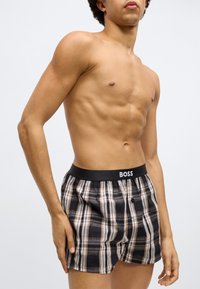 Fekete és bézs kockás boxeralsó, fekete derékpánttal, amelyen "BOSS" logó található, könnyű anyagból és kényelmes szabással.