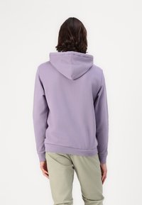 Mikina s kapucňou z jemne fialovej látky, s klokankovým vreckom a rebrovanými manžetami a lemom. Hladký povrch s minimálnym detailom.