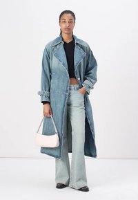 Jeans trenchcoat i lyseblå, med stor krage, knappelukking og lommer. Kombinert med utsvingte lyse jeans og en rosa håndveske.