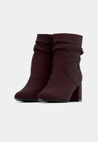 Paire de bottines bordeaux foncé avec tige souple et talons carrés sur un fond clair uni.