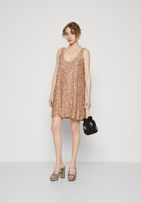 Roze gouden paillettenjurk met een losse pasvorm, ronde halslijn en een lengte tot op de knie. Gecombineerd met metallic platform schoenen en een zwarte handtas.