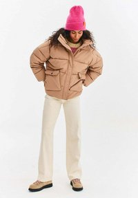 Béžová prešívaná vatovaná bunda s dvoma prednými vreckami, nosená cez pletený sveter. Kombinovaná s krémovými nohavicami a svetlohnedými turistickými topánkami. Ružová pletená čiapka.