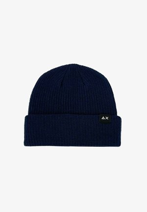 Beanie lavorato a maglia di colore blu navy con una texture a coste e un risvolto. Presenta un'etichetta nera con un design geometrico bianco sul lato.