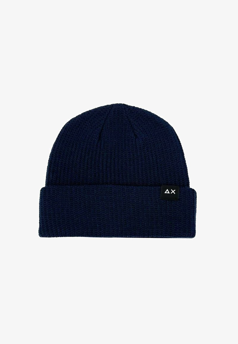 Beanie lavorato a maglia di colore blu navy con una texture a coste e un risvolto. Presenta un'etichetta nera con un design geometrico bianco sul lato.