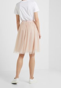 Persona vista di spalle, indossante una t-shirt bianca e una gonna di tulle rosa, abbinata a sneakers bianche in un ambiente minimalista.