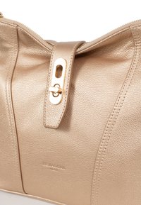 Borsa in ecopelle oro con superficie testurizzata, chiusura con zip e un fermaglio decorativo. Presenta il logo in rilievo "Hexagona Paris".