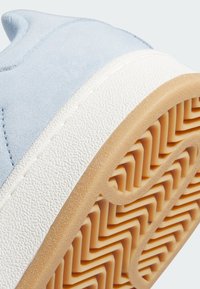 Light blue suede sneaker with white rubber detailing. Textured beige outsole features a zigzag pattern for traction.
