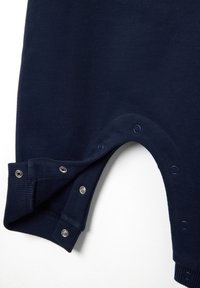 Tela azul marino con botones a presión a lo largo de un borde curvado, parcialmente desabrochados, mostrando un suave forro interior y puños acanalados.