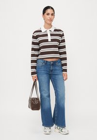 Brun og hvitstripet langermet polo crop top kombinert med lyseblå flarejeans. Tilbehøret inkluderer en brun håndveske og sneakers.