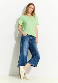 Grøn kortærmet top parret med brede blå denimjeans. Optrækket fuldendes med hvide sneakers med grønne detaljer.