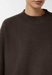 Ciemnobrązowy sweter z okrągłym, prążkowanym dekoltem, wykonany z miękkiego, dzianinowego materiału, o oversize'owym kroju. Bez widocznych wzorów ani zdobień.