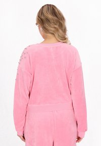 Felpa in velour rosa con spalle abbassate, orlo a costine e decorata con borchie trasparenti sulla spalla sinistra.