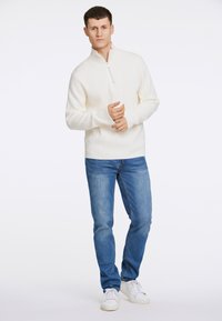 Hvid ribbet quarter-zip sweater parret med lysblå lige-fit jeans og hvide sneakers, med et afslappet design og løs pasform.