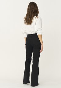 Jeans negre evazați cu talie înaltă și buzunare din spate subtile, asortați cu o cămașă albă cu butoni. Material neted și design ajustat.